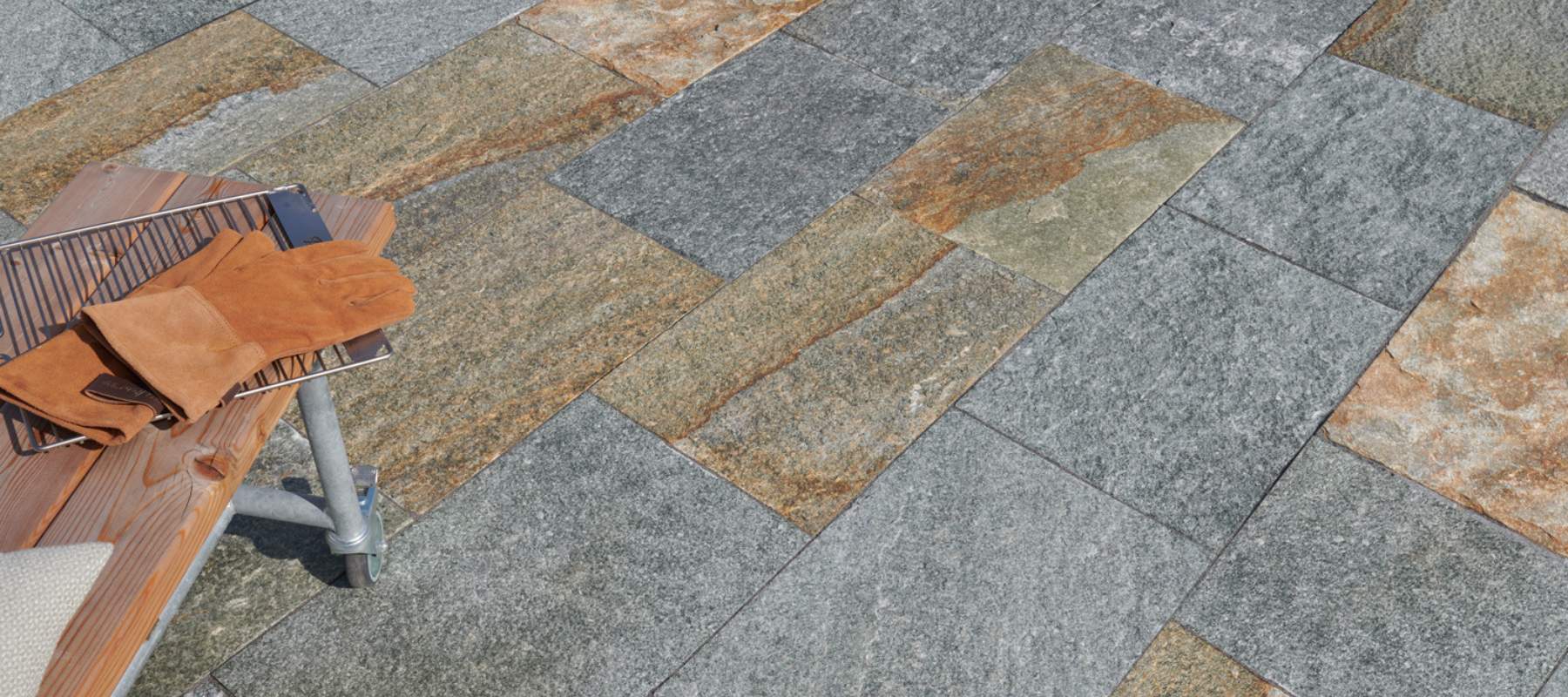 Terrassenfläche aus grauen und goldbraunen Gneisplatten mit Holzbank und Lederhandschuhen