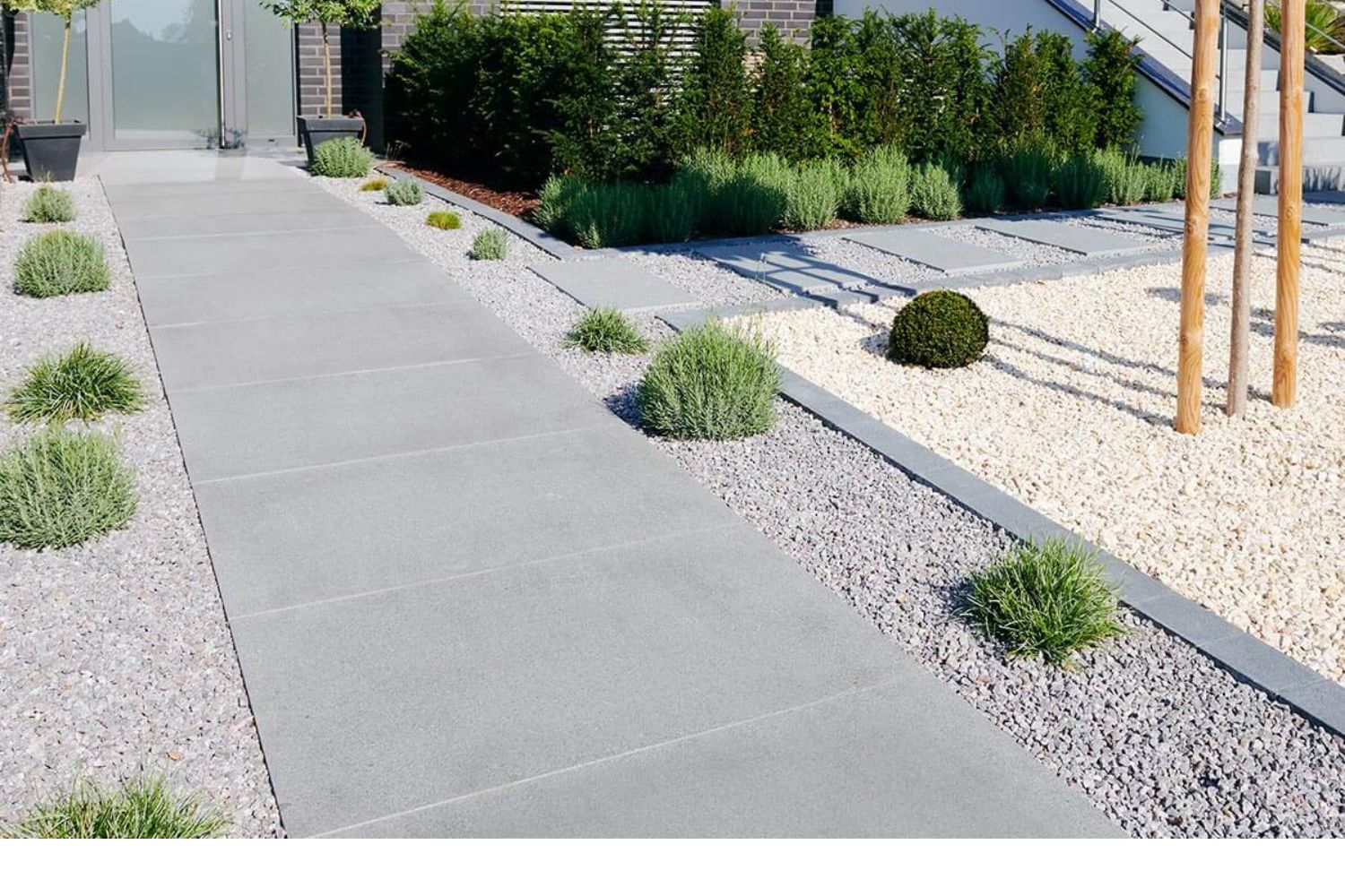 Moderner Hauseingang mit grauen Granitplatten als Gehweg, umgeben von Kiesflächen und minimalistischer Bepflanzung.