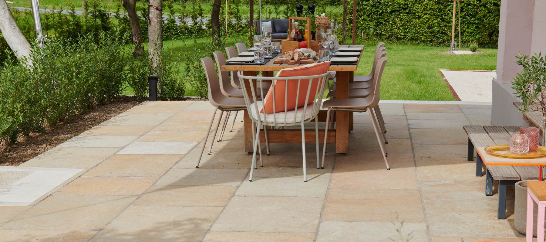 Terrasse mit beigefarbenen Kalksteinplatten, großem Esstisch und modernen Stühlen in einem sonnigen Garten