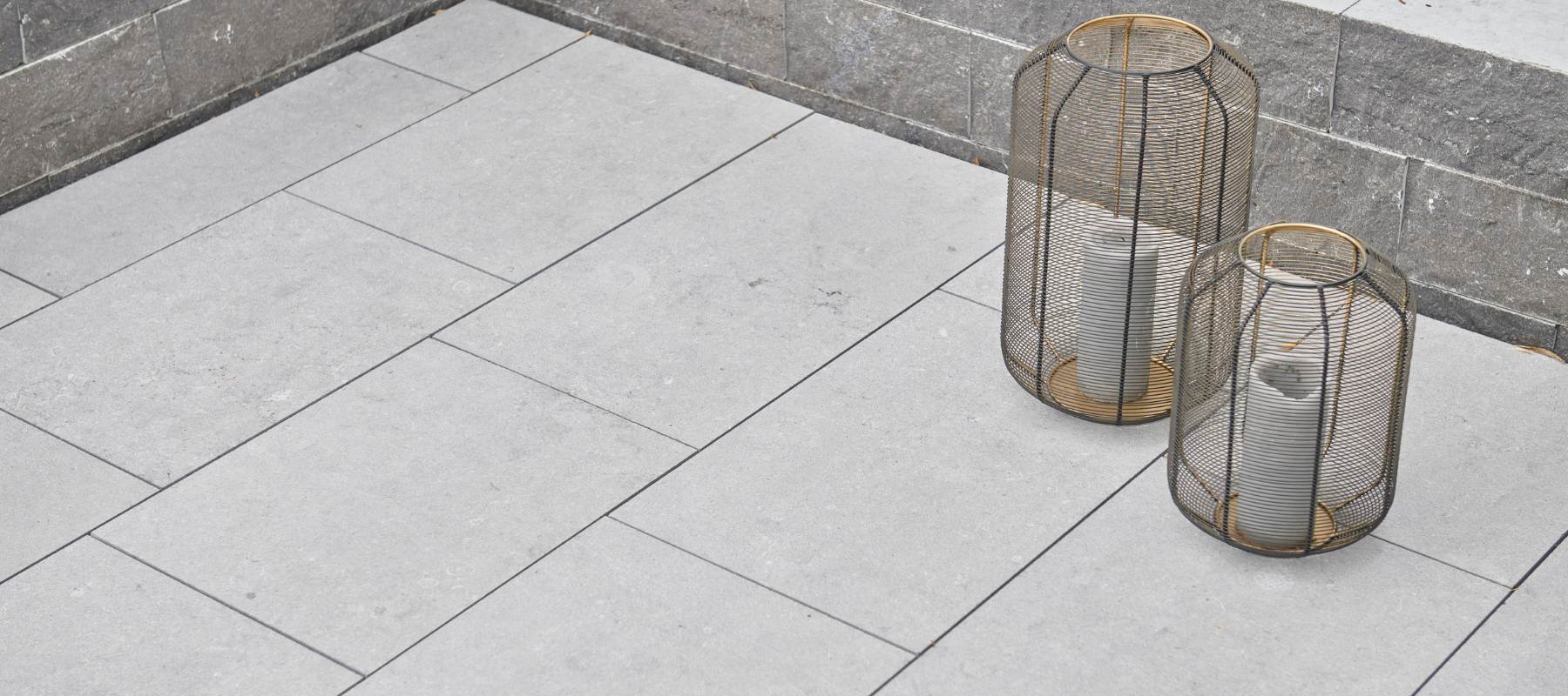 Terrasse mit hellgrauen Kalksteinplatten und zwei dekorativen Metalllaternen mit Kerzen.