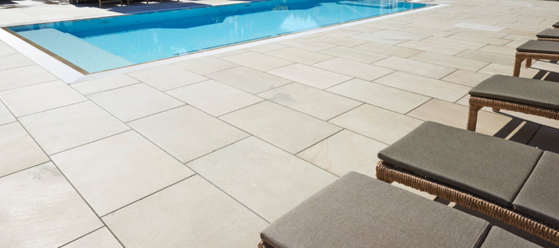Helle Sandstein-Terrassenplatten rund um einen Pool mit Liegestühlen in moderner Gartengestaltung.