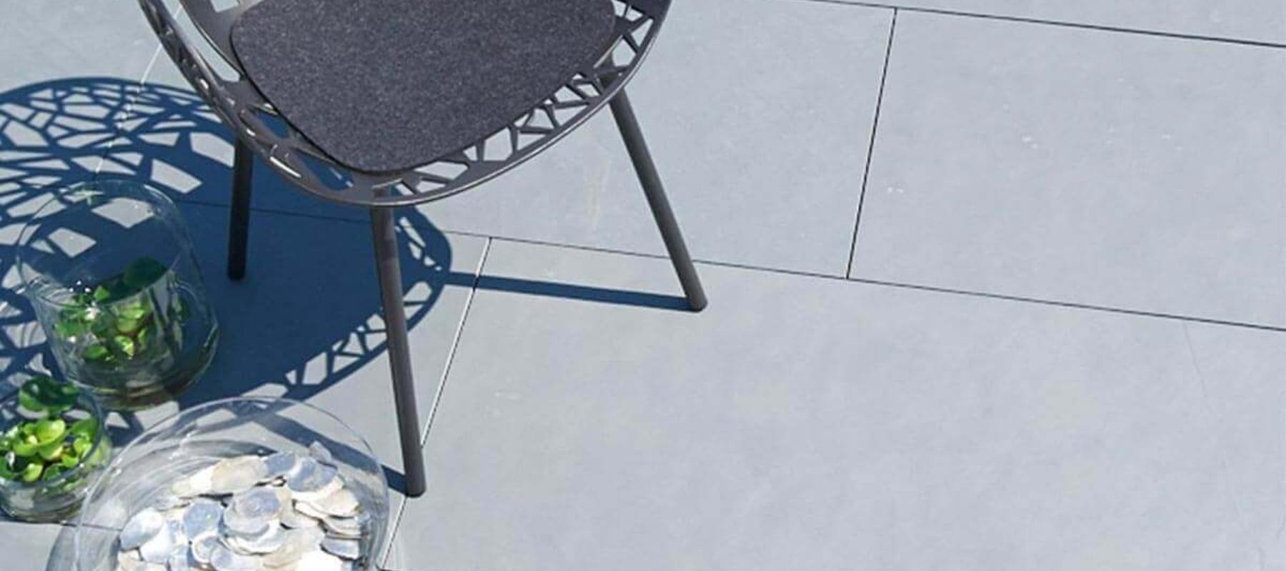 „Terrasse mit hellgrauen Schieferplatten, modernem Stuhl und Glasdekoration im Sonnenlicht.