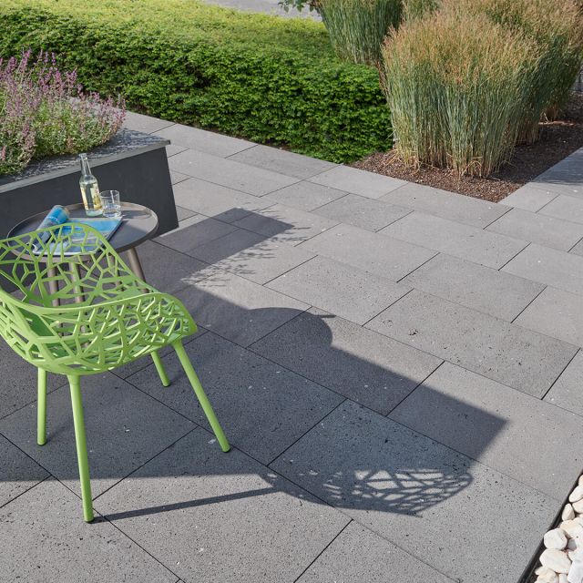 Basanaro® Bodenplatten aus dunkelgrauem Tephrit, rechteckig angeordnet in Bahnen, präsentiert auf weißem Hintergrund. Die offenporige Struktur und der helle Schliff betonen das elegante Design.